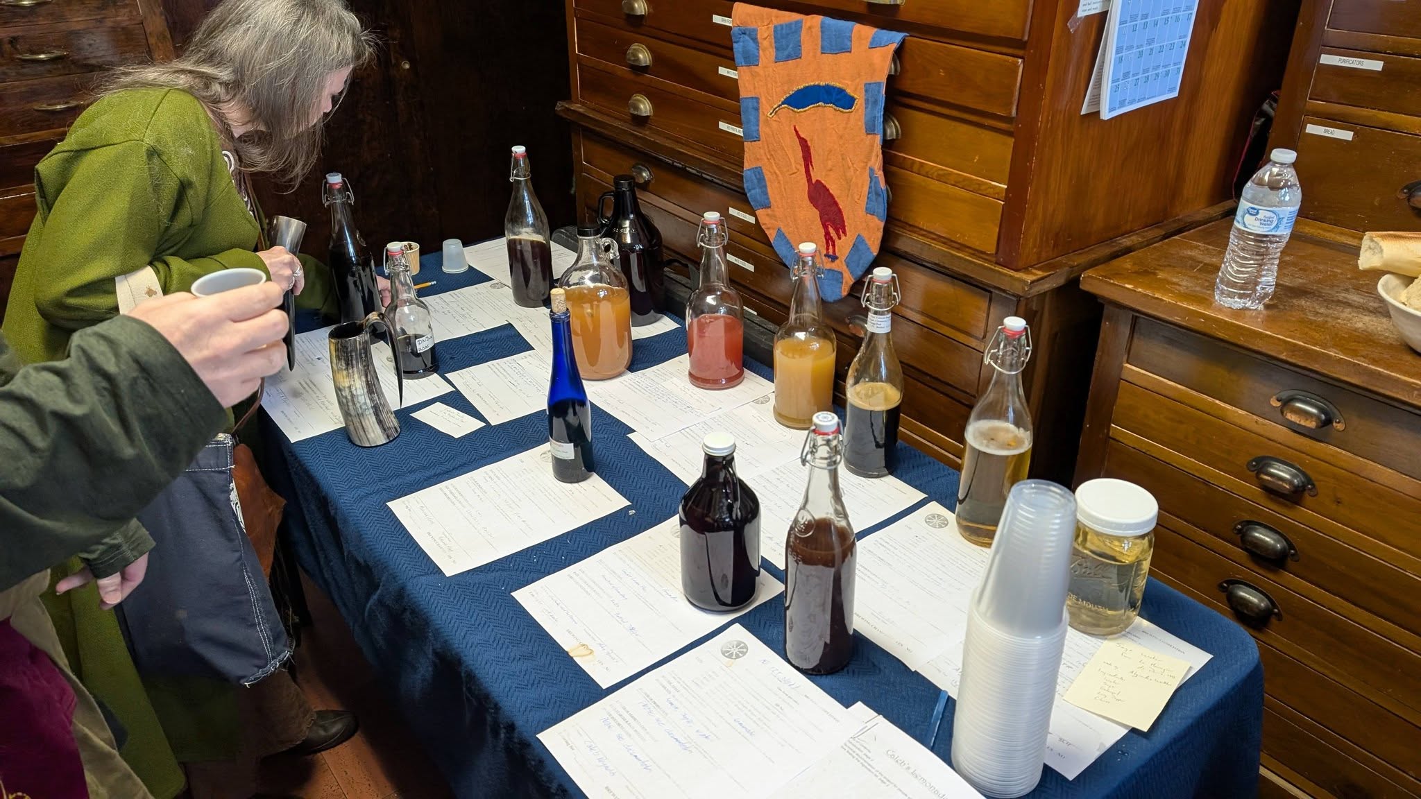 An array of fermented beverages with rubrics arrayed on a table at Kingdom 12th night.